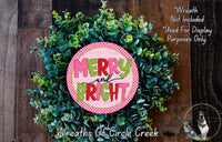 A wreath made of green leaves and a pink circular sign with the text "MERRY and BRIGHT" is displayed on a wooden surface.