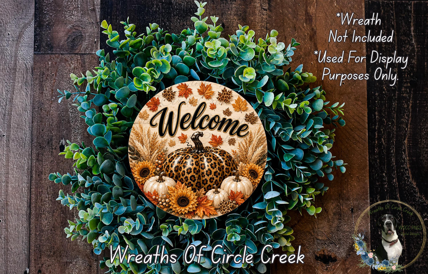 a wreath with a welcome sign, surrounded by various fall-themed elements such as pumpkins, leaves, and sunflowers. The wreath is displayed on a wooden surface, and there is a small dog in the bottom right corner of the image.