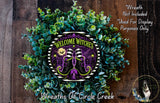 a wreath with a "Welcome Witches" design, surrounded by green foliage. The wreath is displayed on a wooden surface, and there is a small dog in the bottom right corner of the image.