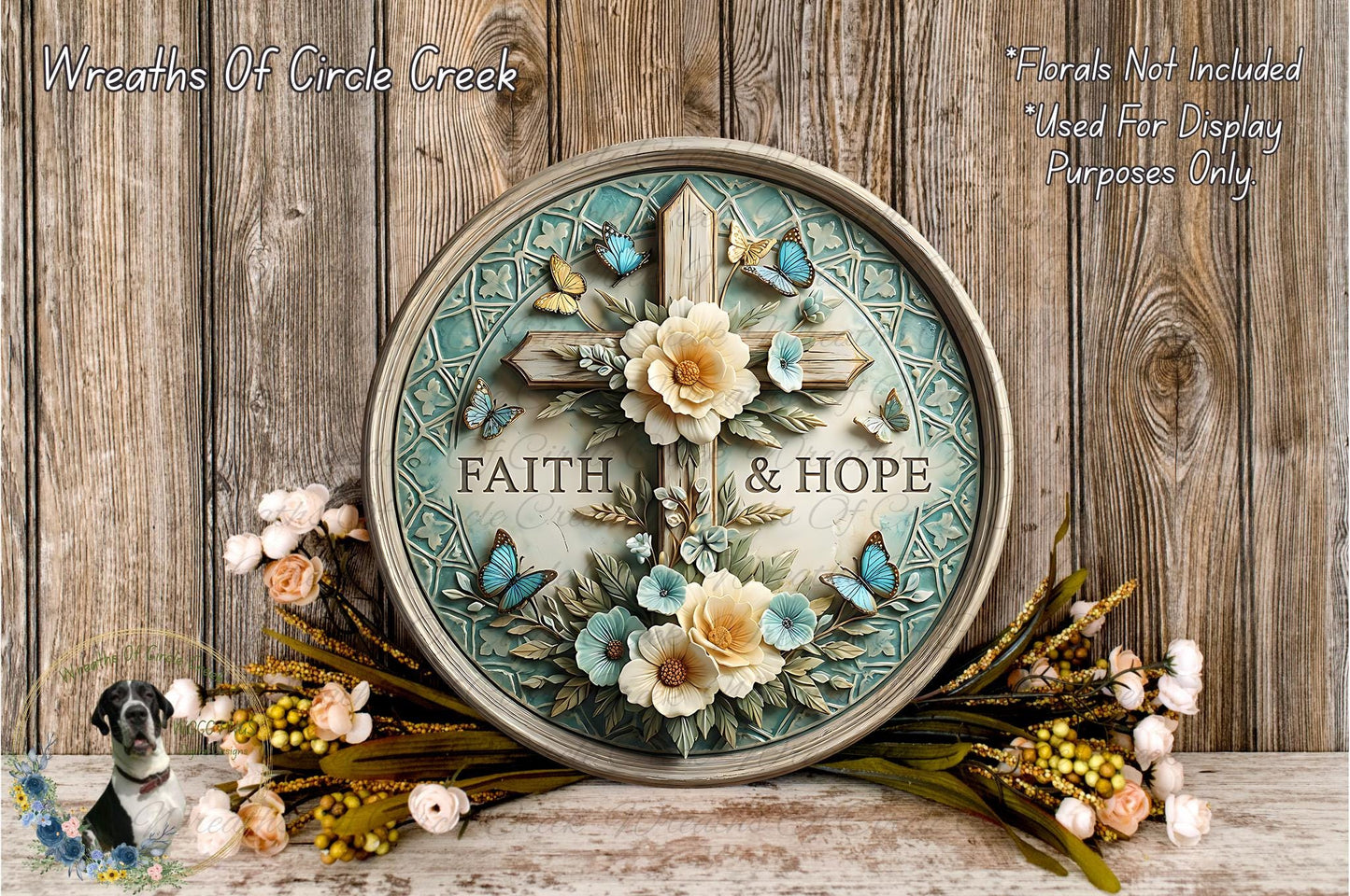 A decorative round wall hanging with a cross and floral elements, surrounded by a wreath of flowers and greenery, placed on a wooden surface.