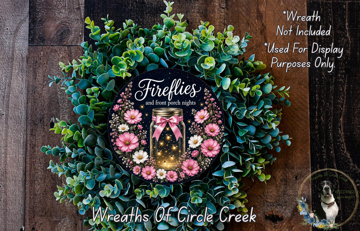 a wreath with a mason jar containing a glowing firefly, surrounded by greenery and pink flowers. The wreath is displayed on a wooden surface, and there is a small dog in the bottom right corner.