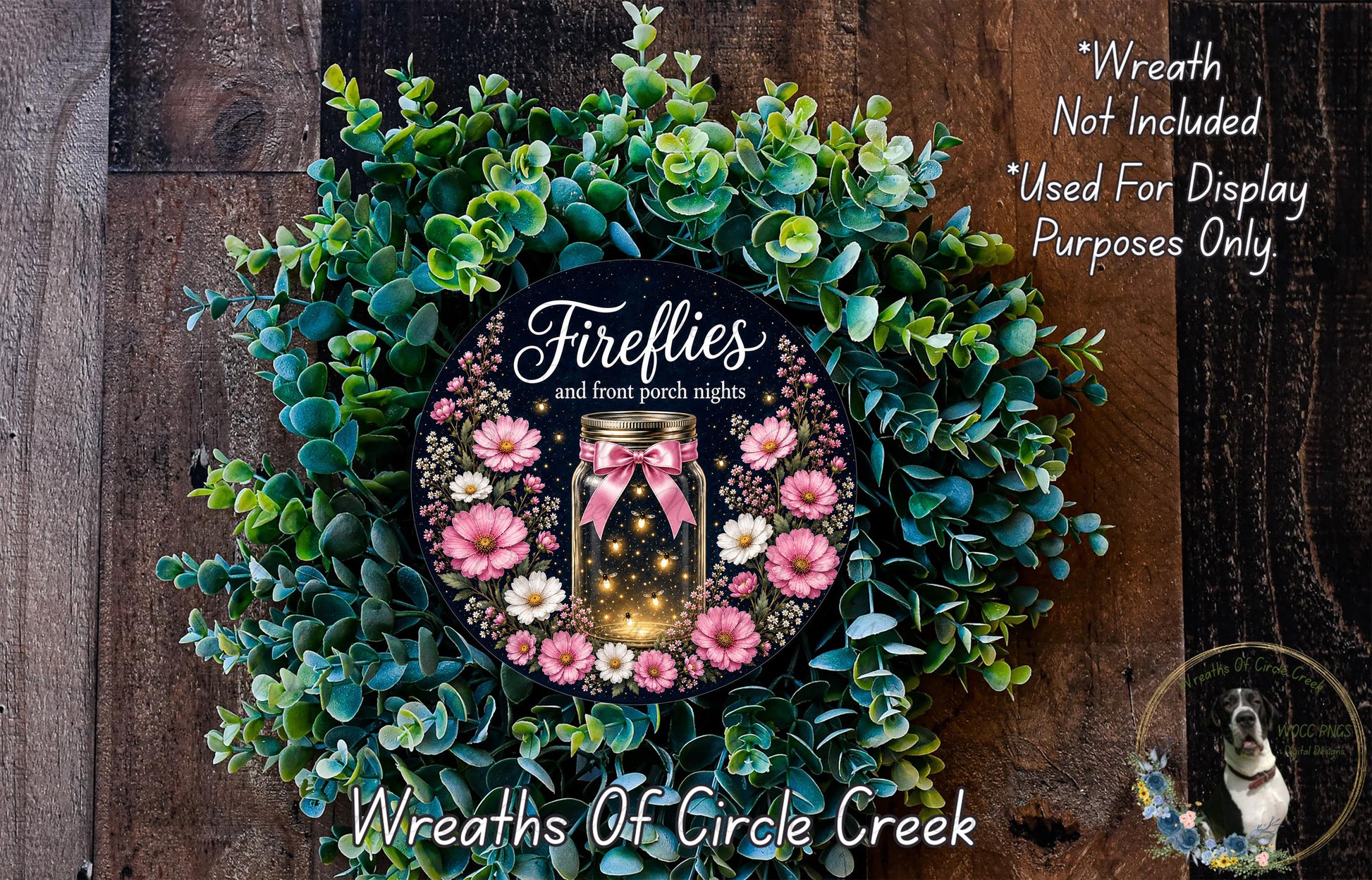 a wreath with a mason jar containing a glowing firefly, surrounded by greenery and pink flowers. The wreath is displayed on a wooden surface, and there is a small dog in the bottom right corner.