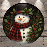A snowman wearing a black top hat and a red and black plaid scarf, surrounded by holly leaves and berries, is depicted in the image.