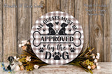 a round wooden sign with the text "All guests must be approved by the dog" and a dog silhouette. The sign is surrounded by a floral arrangement and placed on a wooden surface.