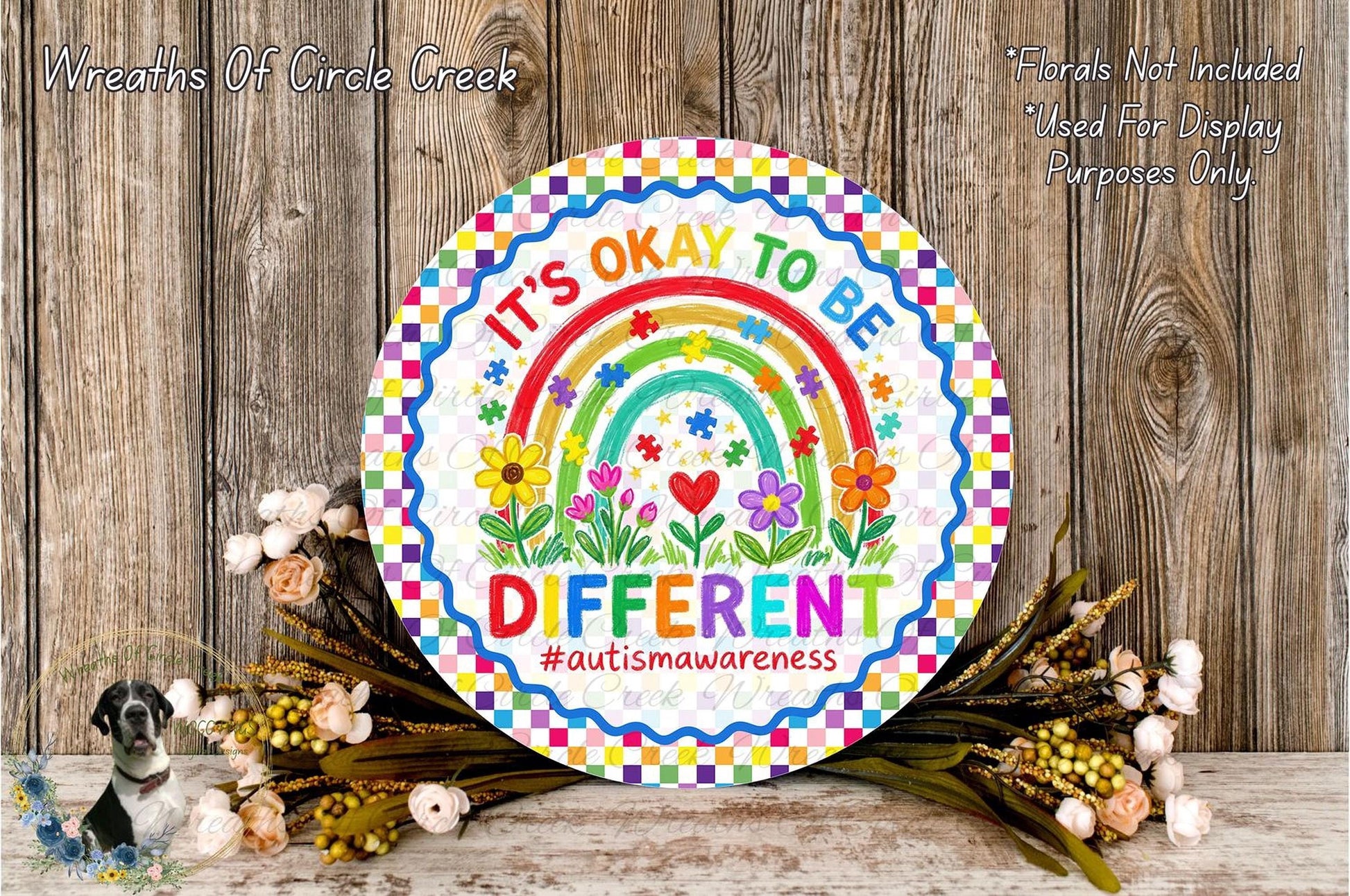 A colorful sign with a rainbow and flowers, along with the text "It's OK to be DIFFERENT #autismawareness" is displayed on a wooden surface.