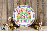 A colorful sign with a rainbow and flowers, along with the text "It's OK to be DIFFERENT #autismawareness" is displayed on a wooden surface.