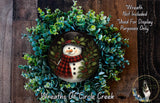 A wreath made of green foliage and featuring a snowman as the central figure.