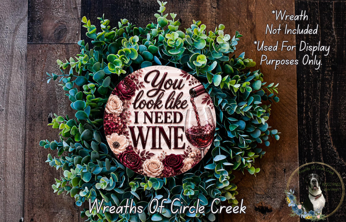 A wreath made of green leaves and flowers, with a circular sign that says "You look like I need wine".