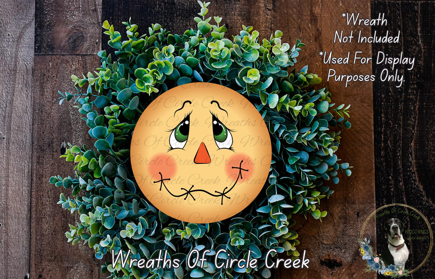 A wreath made of green plants and a yellow face with a red nose, resembling a scarecrow or scarecrow face, is displayed on a wooden surface.