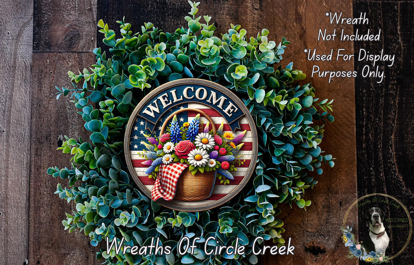a wreath with a patriotic design, including a basket of flowers and a "Welcome" sign. The wreath is surrounded by greenery and placed on a wooden surface.