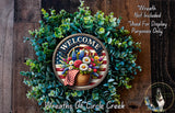 a wreath with a patriotic design, including a basket of flowers and a "Welcome" sign. The wreath is surrounded by greenery and placed on a wooden surface.