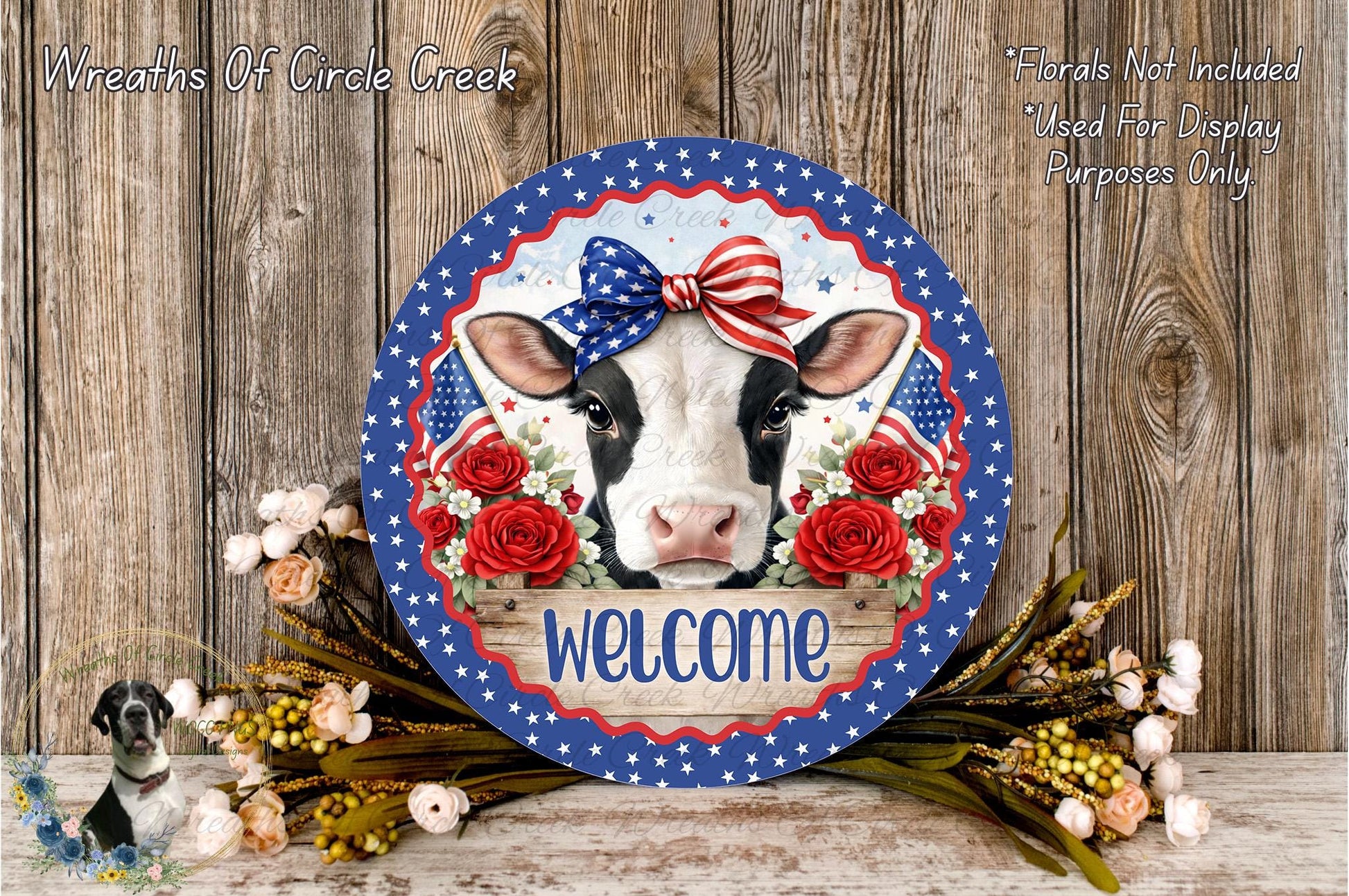 a decorative sign with a cow's face, surrounded by flowers and a bow, placed on a wooden surface.
