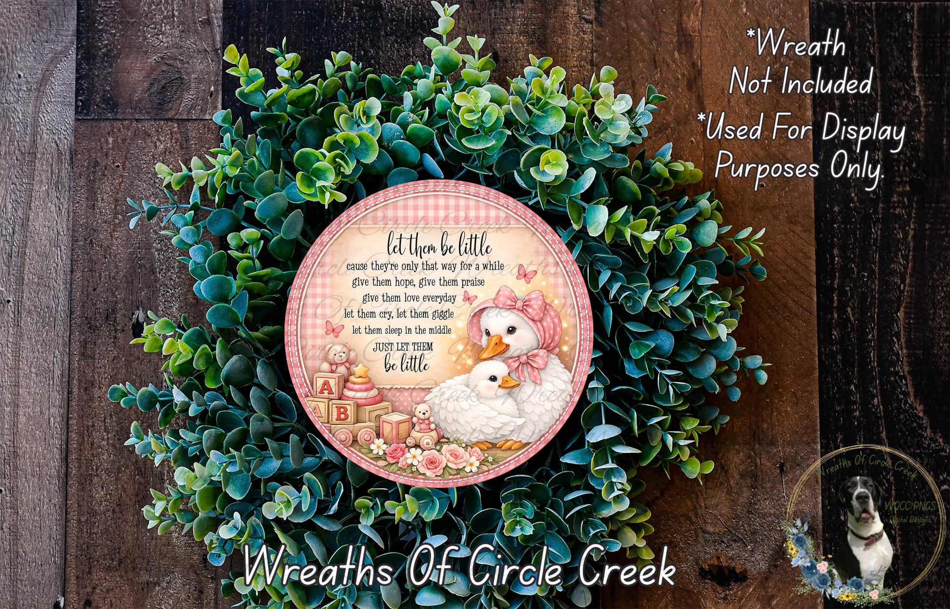 a wreath made of green leaves and a pink and white decorative plate with a baby bird and a letter "A" on it, placed on a wooden surface.