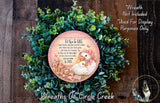 a wreath made of green leaves and a pink and white decorative plate with a baby bird and a letter "A" on it, placed on a wooden surface.