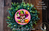 A wreath made of green leaves and a colorful skull wearing a hat, with a pumpkin and other decorative elements.