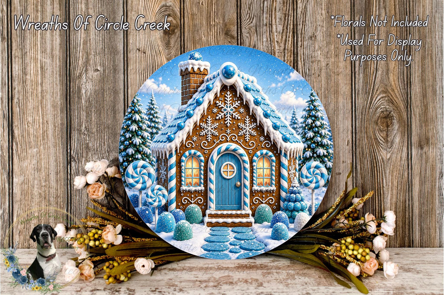 A round wooden plaque depicting a gingerbread house with a blue door and windows, surrounded by a wreath of flowers and a snowy landscape.
