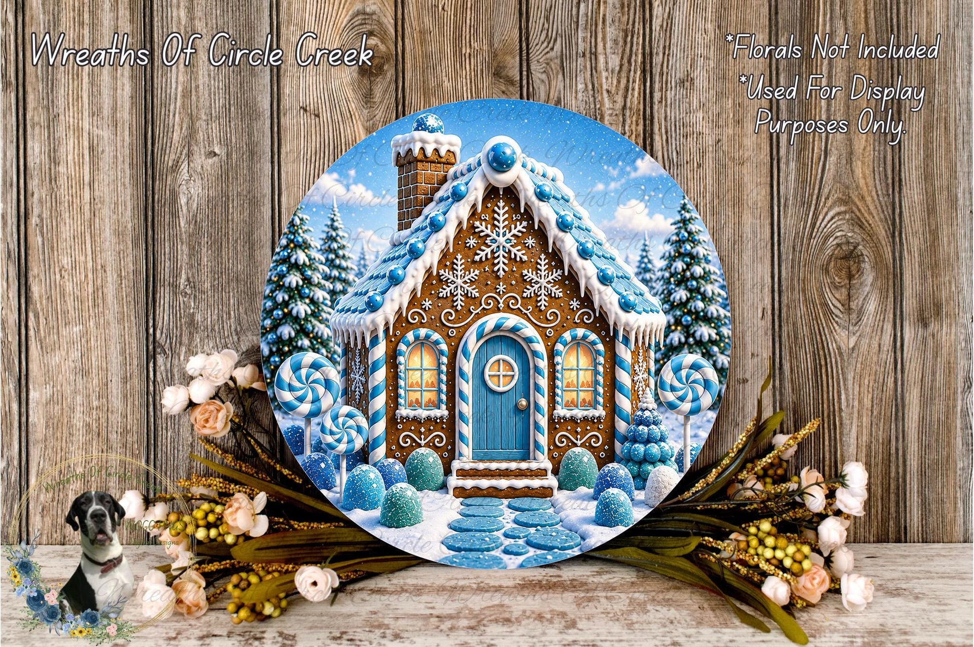 A round wooden plaque depicting a gingerbread house with a blue door and windows, surrounded by a wreath of flowers and a snowy landscape.