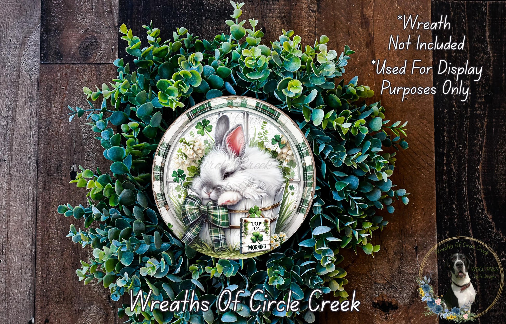 A wreath made of green leaves and flowers, with a white rabbit depicted in the center. The wreath is displayed on a wooden surface, and there is a text overlay that reads "Wreath Not Included * Used For Display Purposes Only".