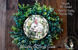 A wreath made of green leaves and flowers, with a white rabbit depicted in the center. The wreath is displayed on a wooden surface, and there is a text overlay that reads &quot;Wreath Not Included * Used For Display Purposes Only&quot;.