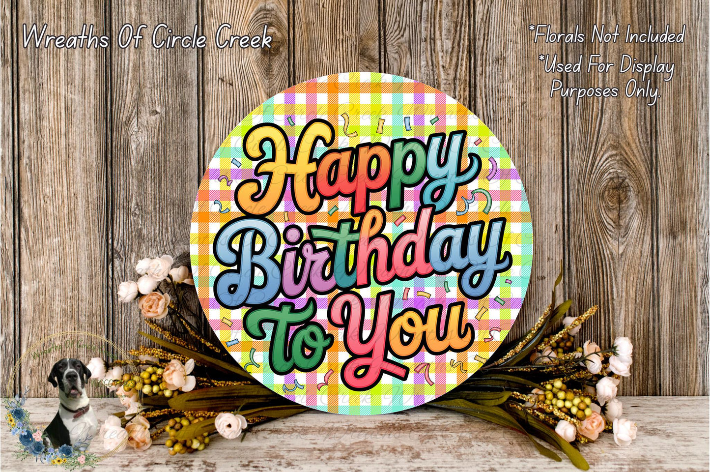 A colorful birthday wreath with the text "Happy Birthday to You" displayed on it, surrounded by flowers and placed on a wooden surface.