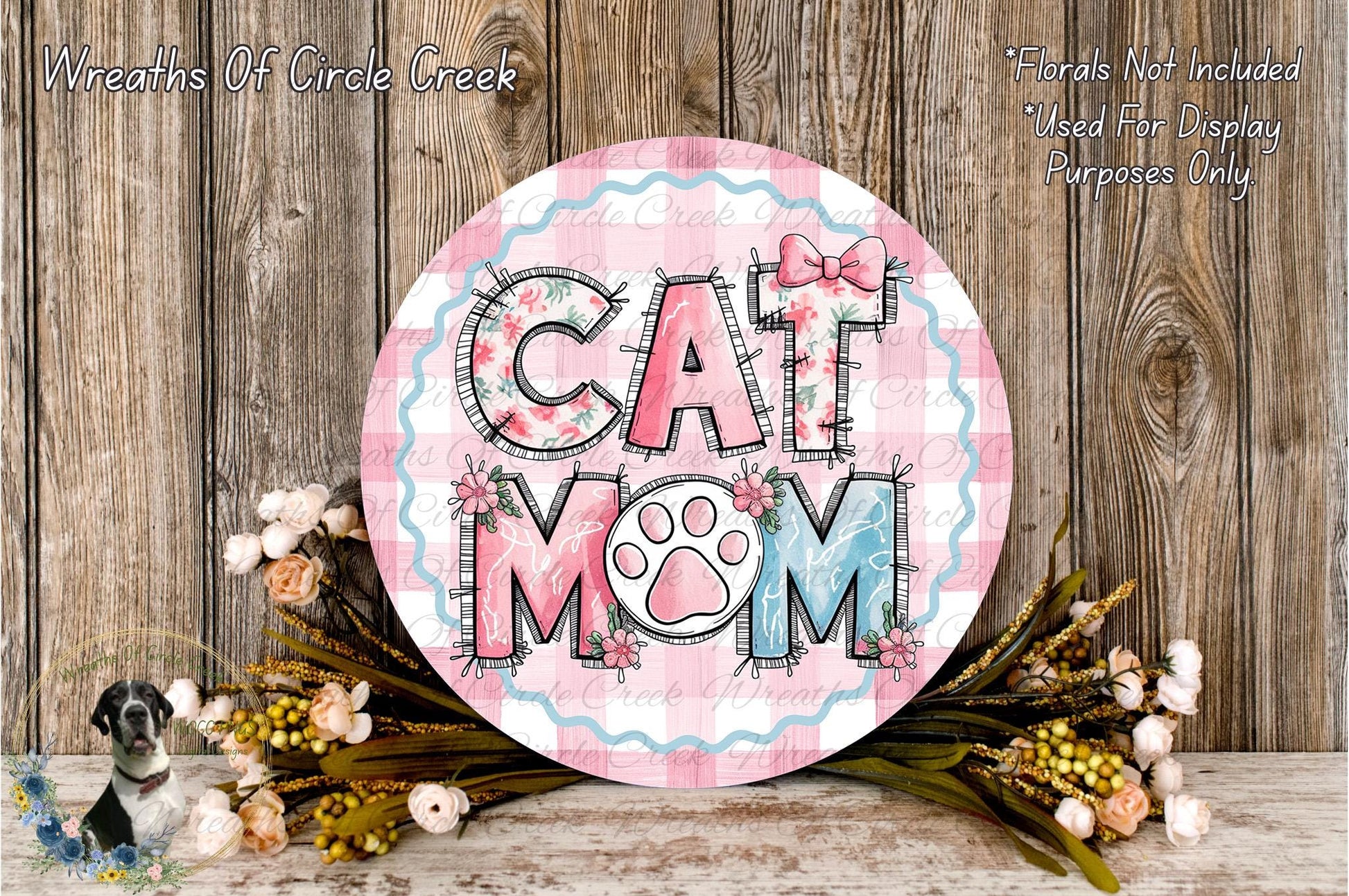 A decorative sign with the text "CAT MOM" in a floral design, surrounded by a bouquet of flowers and a wooden background.