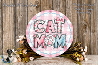 A decorative sign with the text "CAT MOM" in a floral design, surrounded by a bouquet of flowers and a wooden background.