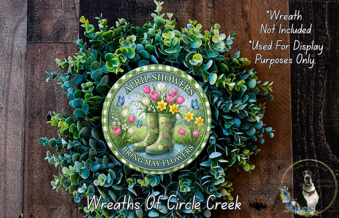 a wreath made of various green plants and flowers, including tulips and daisies, with a circular sign in the center that reads "April Showers Bring May Flowers".