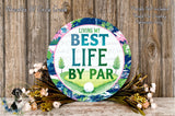 a decorative plate with the text "LIVING MY BEST LIFE BY PAR" surrounded by a floral arrangement on a wooden surface.