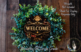 a wreath with the word "WELCOME" prominently displayed in the center. The wreath is made of various green and brown foliage, creating a festive and welcoming atmosphere. The background of the image is a wooden wall, which complements the wreath and adds to the overall aesthetic.