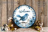 a round blue and white sign with a blue bird perched on a branch, surrounded by flowers and greenery. The sign has the word "Welcome" written on it.