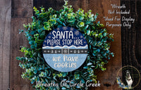 A wreath made of green leaves and a blue sign with text, placed on a wooden surface.