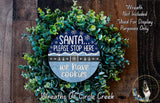 A wreath made of green leaves and a blue sign with text, placed on a wooden surface.