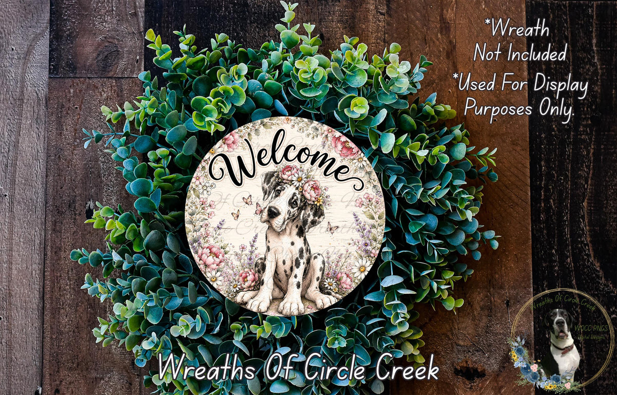 a wreath with a dog in the center, surrounded by various green plants and flowers. The wreath is displayed on a wooden surface, and there is a text overlay that reads "Welcome Wreath Not Included * Used For Display Only. Purposes Only."