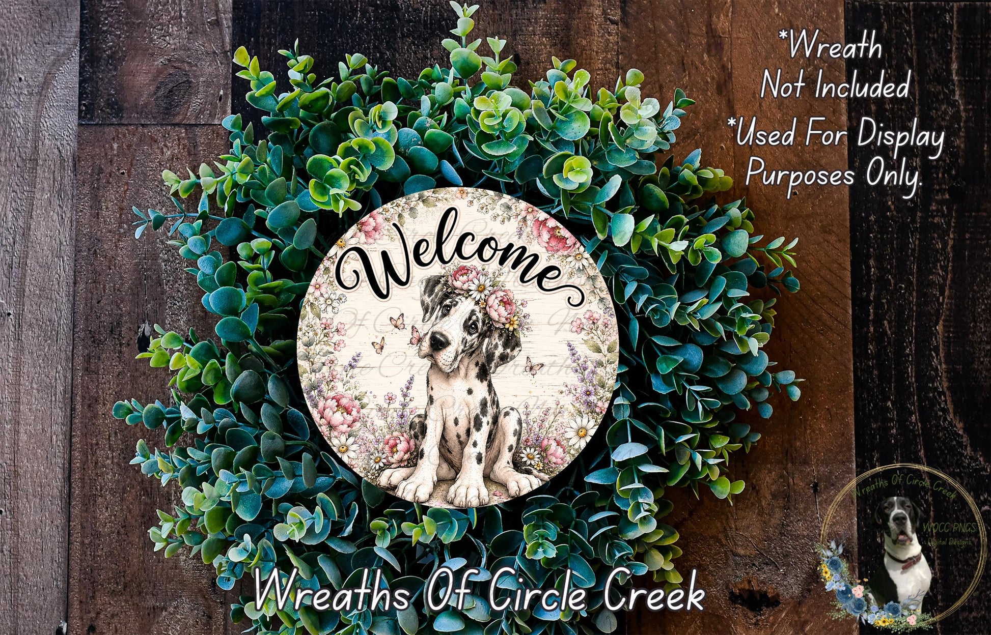 a wreath with a dog in the center, surrounded by various green plants and flowers. The wreath is displayed on a wooden surface, and there is a text overlay that reads "Welcome Wreath Not Included * Used For Display Only. Purposes Only."