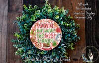 A wreath made of green leaves and decorated with various holiday-themed items, including a sign that says "Santa we have the best cookies".