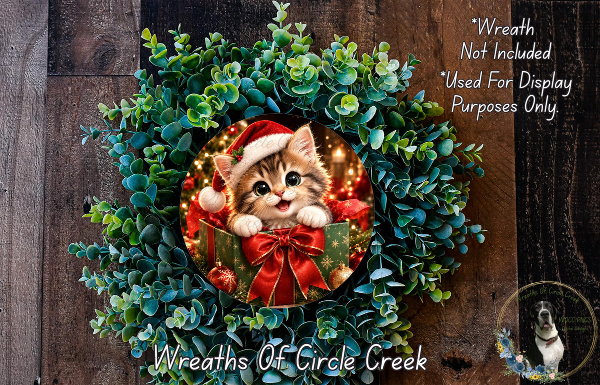 A wreath made of green plants and a small kitten wearing a Santa hat, with a red bow around its neck.