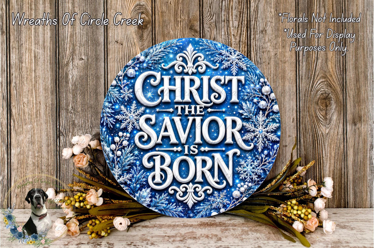 A blue circular sign with the text "CHRIST THE SAVIOR IS BORN" surrounded by snowflakes and flowers, placed on a wooden surface.