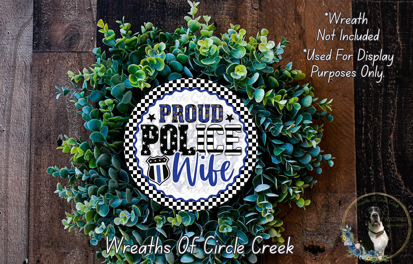 a wreath made of green leaves and flowers, with a circular sign that reads "Proud Police Wife" in bold letters. The wreath is displayed on a wooden surface, and there is a small dog visible in the bottom right corner of the image.
