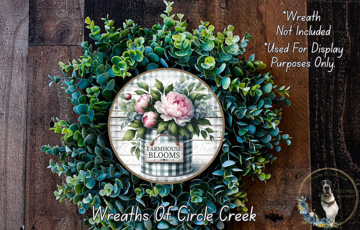 a wreath made of various green plants and flowers, including a large floral arrangement in the center. The wreath is displayed on a wooden surface, and there is a small sign or text that reads "Wreath Not Included * Used For Display Purposes Only".