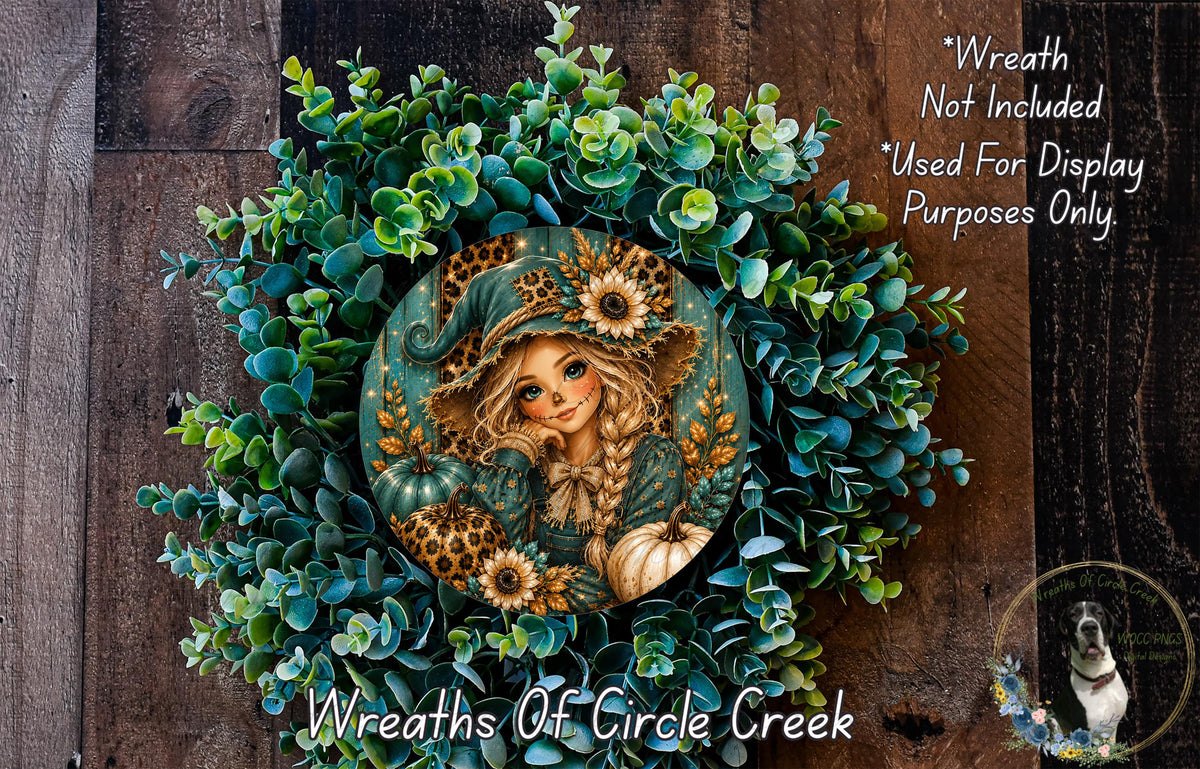 a wreath with a woman's face and a cat, surrounded by green leaves and pumpkins. The wreath is displayed on a wooden surface, and there is a small dog in the bottom right corner of the image.
