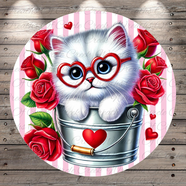 A white cat wearing red glasses is sitting inside a bucket filled with red roses, surrounded by additional red roses.