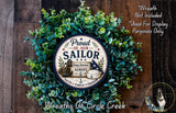 A wreath made of green leaves and a circular sign with the text "Proud of our Sailor" and an illustration of a sailor.