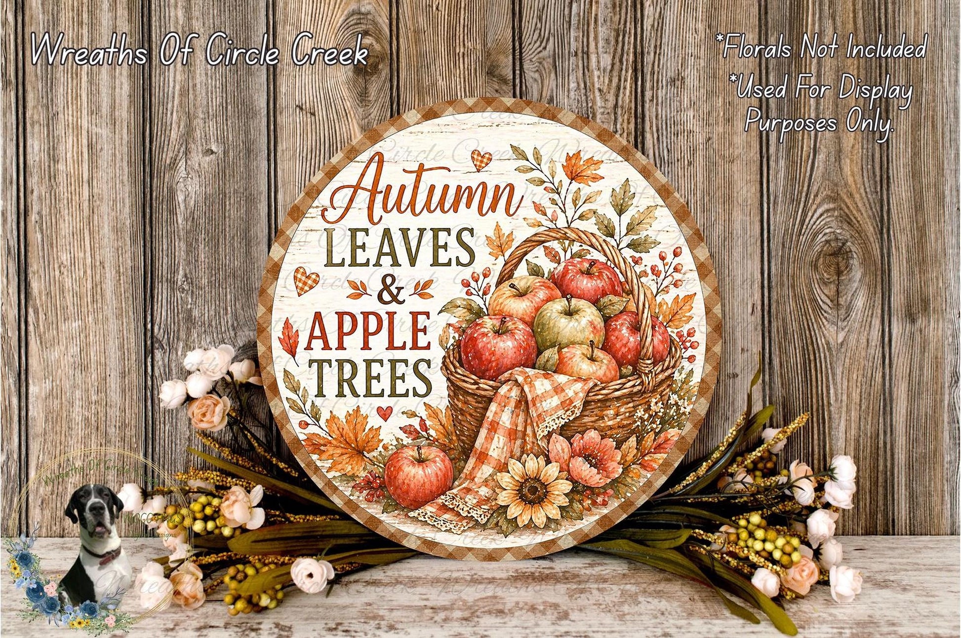 a round wooden sign with a decorative design, surrounded by autumn-themed decorations such as flowers and leaves, and a basket of apples.