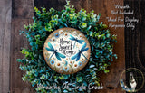 a wreath made of various green plants and flowers, with a wooden sign in the center that says "Home Sweet Home".