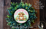 a wreath made of green foliage and a decorative plate with a cartoon image of a bunny holding a basket of Easter eggs. The plate is labeled "The Golden Bunny Bakery" and is surrounded by a lush, natural-looking wreath.