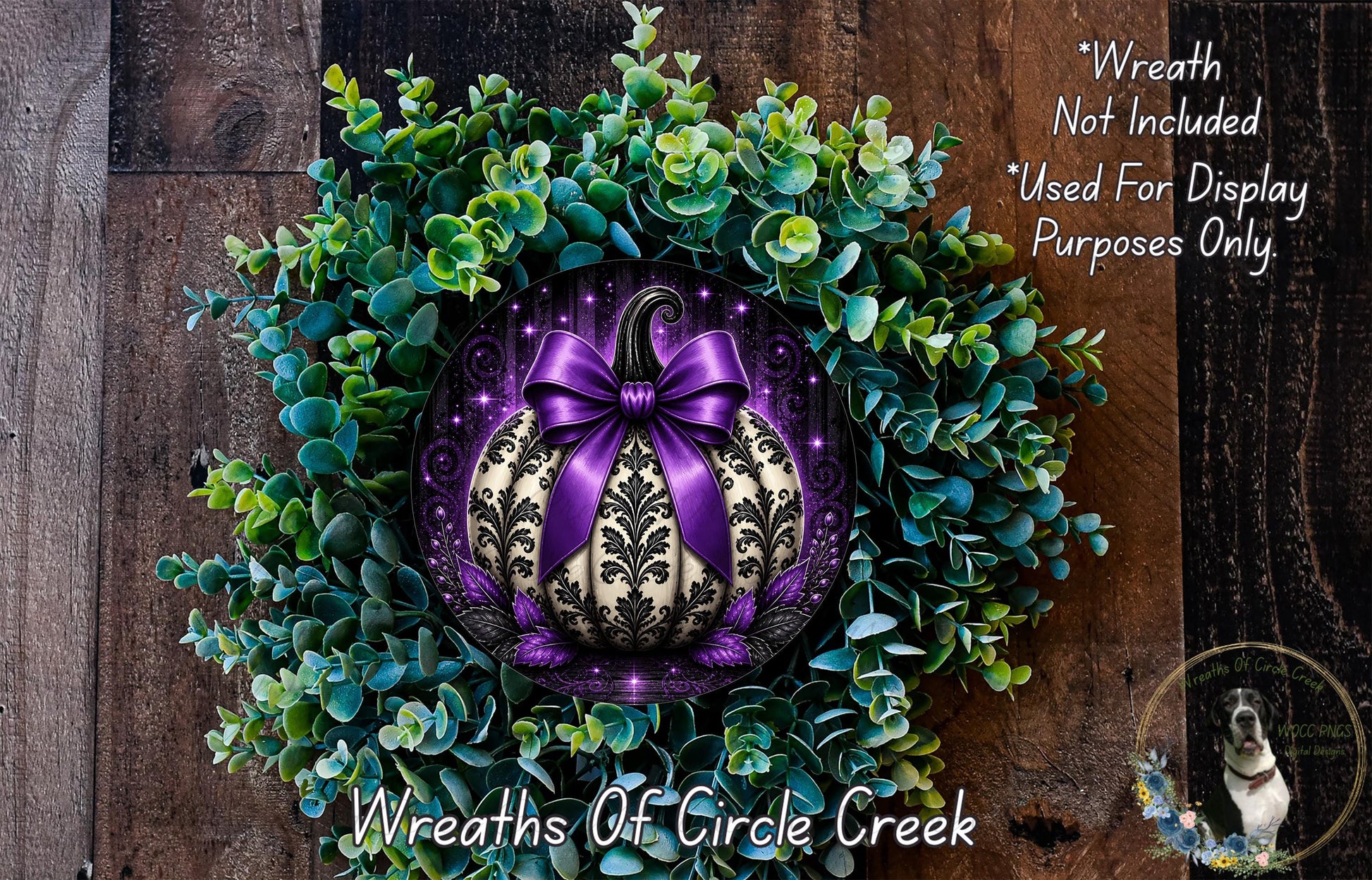 a wreath with a purple bow and a black and white pumpkin design, surrounded by green foliage. The wreath is displayed on a wooden surface, and there is a small dog in the bottom right corner of the image.