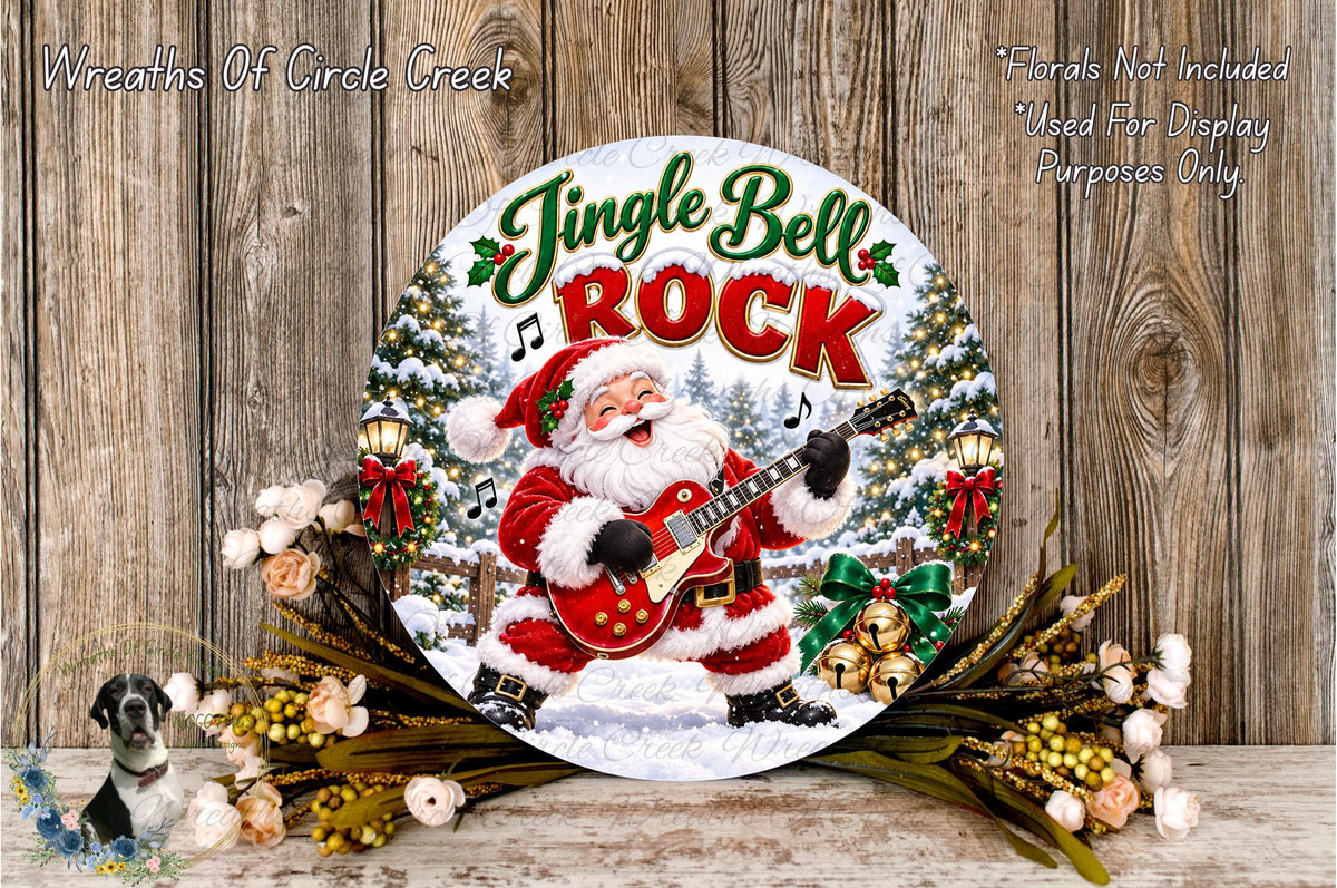 A round metal sign with a jingle bell and rock theme, featuring a Santa Claus figure playing a guitar. The sign is surrounded by holiday decorations, including flowers and greenery, and is displayed on a wooden surface.