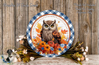 A decorative plate featuring an owl surrounded by autumn foliage, flowers, and a checkered border. The plate is placed on a wooden surface, and there are additional flowers and foliage nearby.