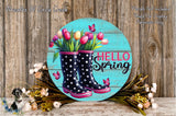 A round wooden sign with a floral design, featuring a pair of black and pink polka dot rain boots surrounded by a bouquet of colorful flowers and butterflies.