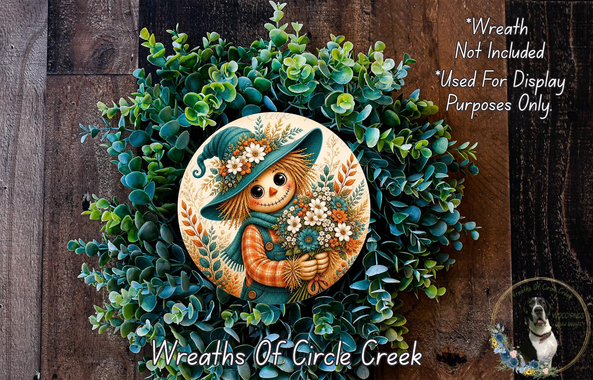 a wreath with a scarecrow design, surrounded by a lush green wreath. The wreath is displayed on a wooden surface, and there is a small dog in the bottom right corner of the image.